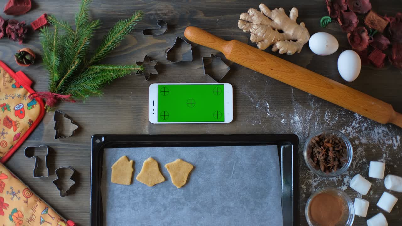 A woman lays out Christmas gingerbread cookies whit green screen smartphone. Cookie making training.