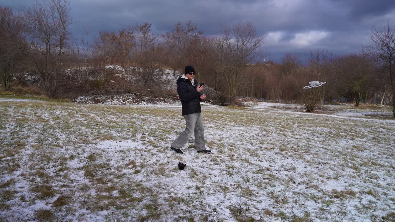 Man walking backward with drone controller in snowy field, Czech Republic