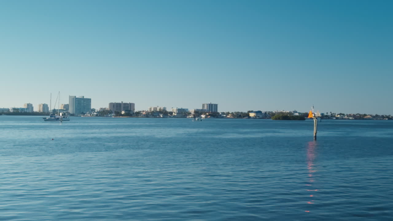 Clearwater skyline appears across calm blue water with subtle boat silhouettes drifting across the quiet Saint Joseph Sound, pan right establish