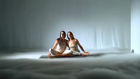 two women performing a synchronized partner yoga pose in a misty studio