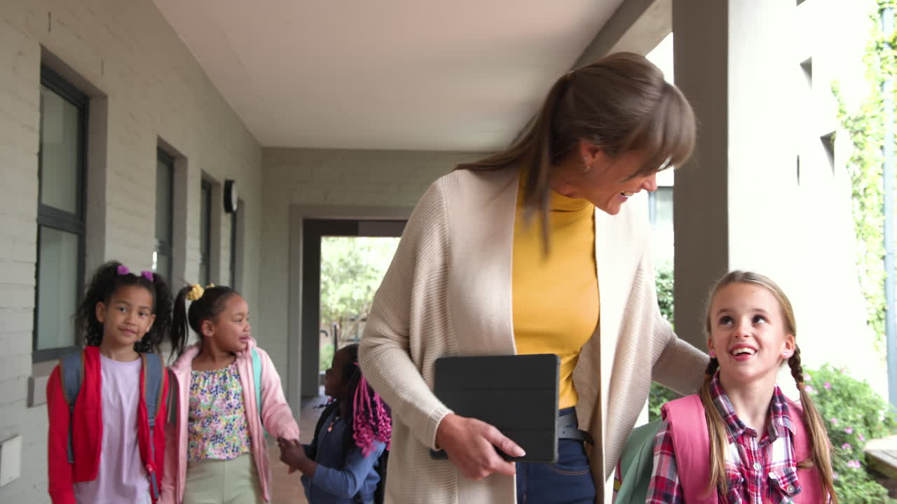 Walking with students at school, teacher holding tablet, having conversation