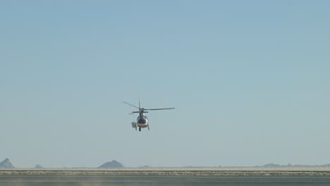 A-helicopter-flying-into-the-desert-at-the-Dakar-rally,-desert-landscape-and-blue-sky