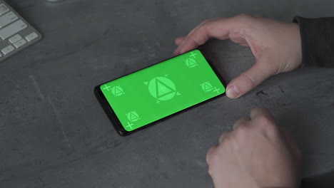 holding smartphone with horizontal green screen chroma, reading, touching. mockup.