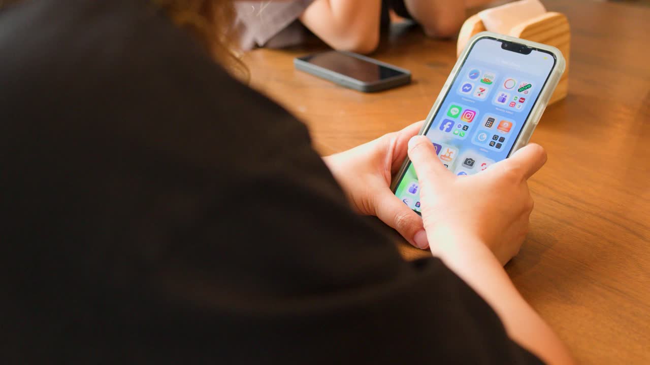 A person scrolls through apps on a smartphone while sitting at a wooden cafe table