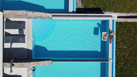 down view of woman sitting by pool and sunbathing while enjoying food and drink