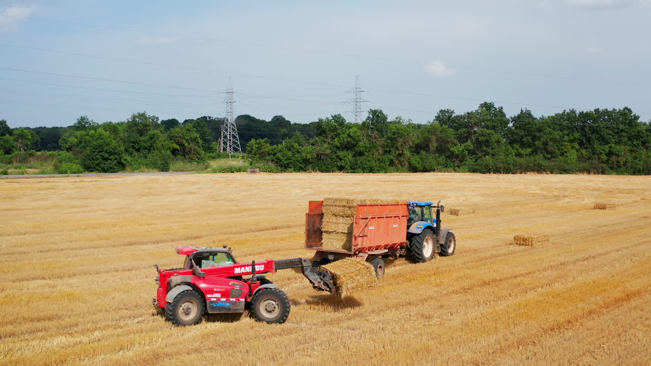 Little excavator picking hay bales and loading them on the tractor. Approaching to the tractor machine full of straw harvest.