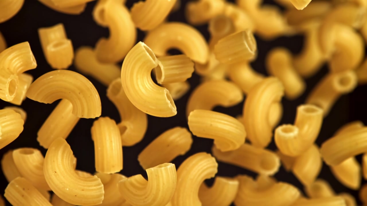 Primo piano di maccheroni a gomito secchi che cadono al rallentatore