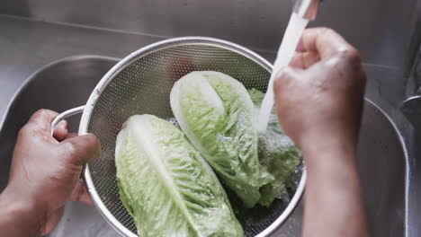 African-american-male-chef-washing-vegetables-in-sink-in-kitchen,-slow-motion