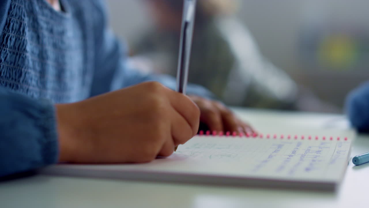 Girl writing in notebook at desk in classroom. Student doing classwork at school