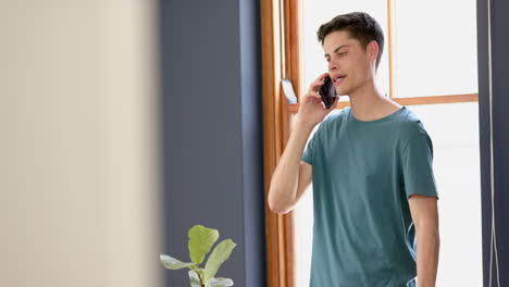 happy biracial man talking on smartphone standing in sunny living room, copy space, slow motion