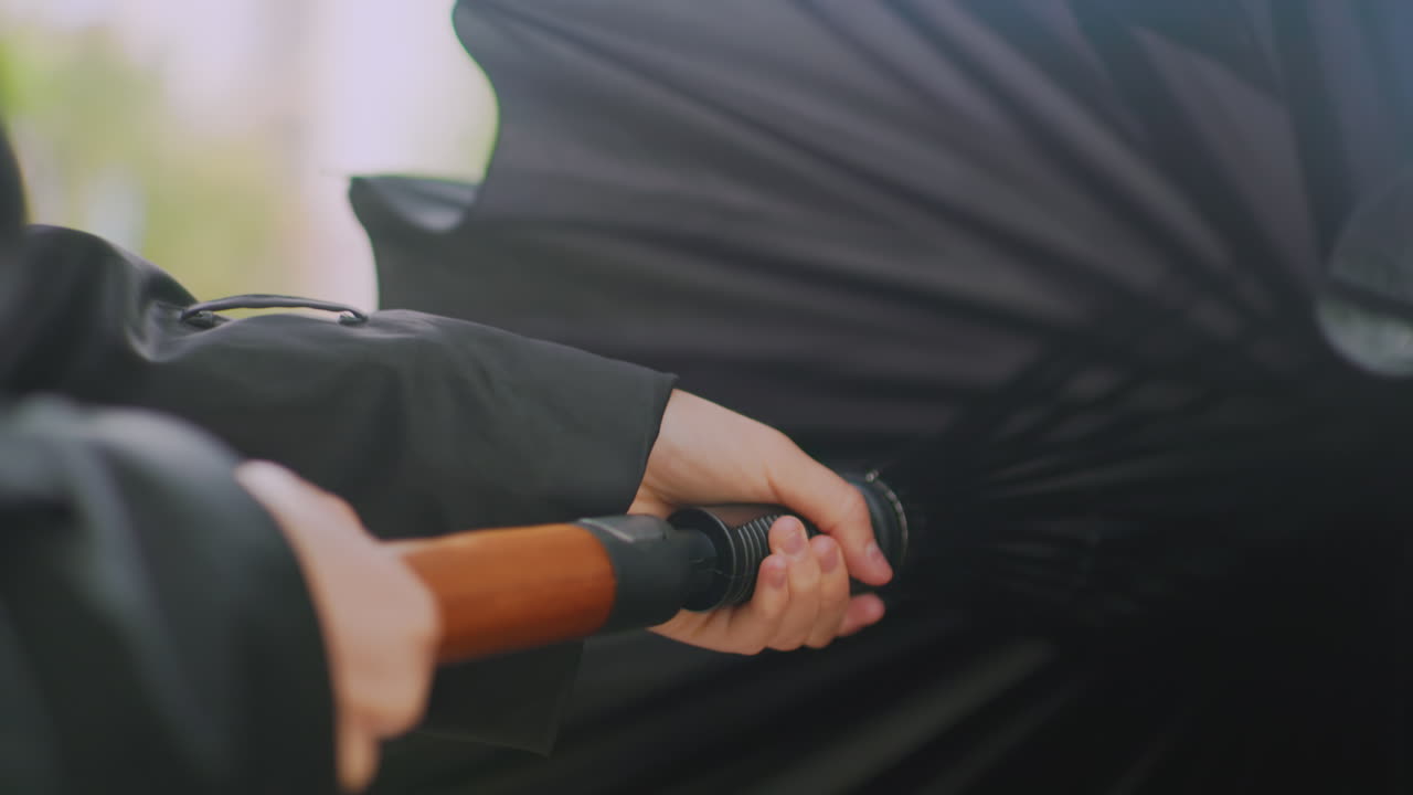 Close up of hand holding black umbrella from inside view, showing structure of ribs and handle, person gripping firmly for rain protection, concept of shelter, safety, dark fabric background