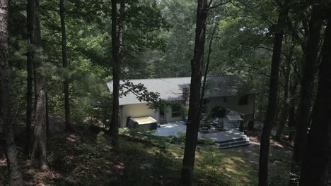 pov: rural house on forested country hillside seen through green trees