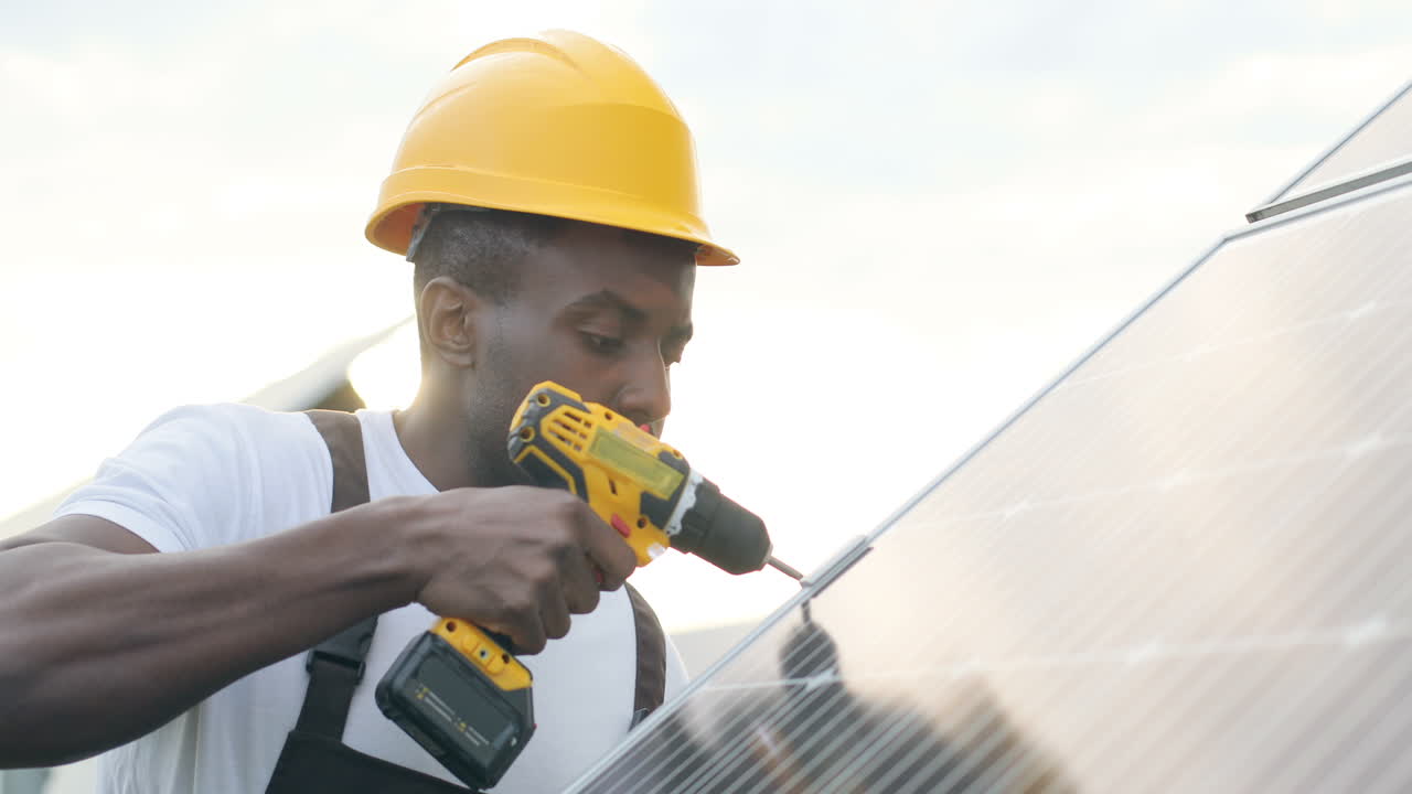 Close-up view of african american man in special uniform and protective helmet repairing a solar panel