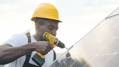 vista cercana del hombre afroamericano en uniforme especial y casco protector reparando un panel solar