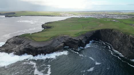 dramáticos acantilados de kilkee y costa con olas estrelladas y campos verdes, bajo un cielo nublado, vista aérea