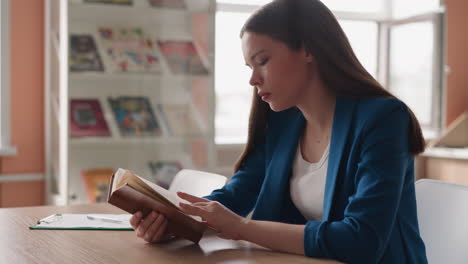 woman flips through pages of old book in library. lady reads vintage novel at desk in college engaged in literature work for essay. studying woman closeup