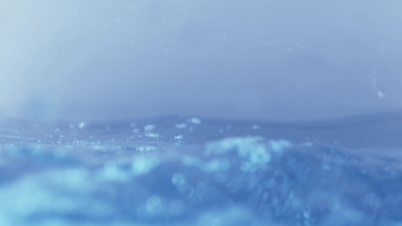 슬로우 모션의 깨끗한 물 표면은 물이 튀는 상점으로 화면을 채우고 기포로 액체 표면을 흔들고 있습니다.