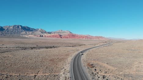 Aerial-drone-shot-of-Red-Rock-Scenic-Highway-with-mountains-in-the-background