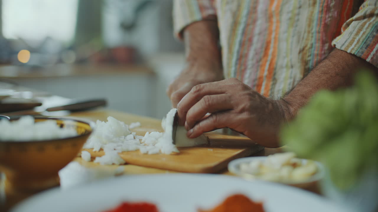 primer plano de las manos de un hombre cortando cebollas en una tabla de madera en la mesa de la cocina