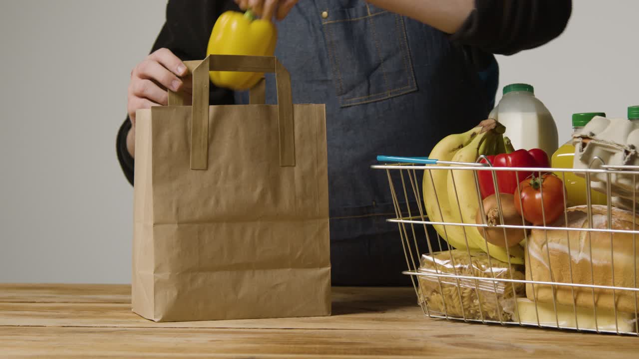 foto de estudio de un trabajador de la tienda empacando alimentos básicos en una cesta de compras de alambre de supermercado en una bolsa de papel 4