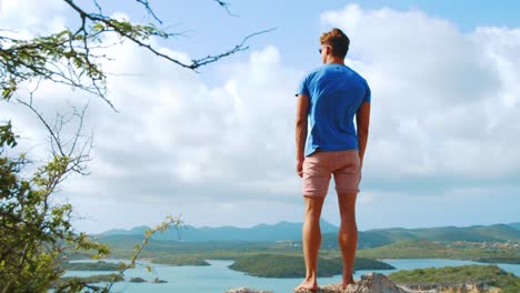 Blick-Von-Hinten-Auf-Den-Jungen-Mann,-Der-Am-Aussichtspunkt-In-Curacao-Mit-Blick-Auf-Die-Bucht-Steht