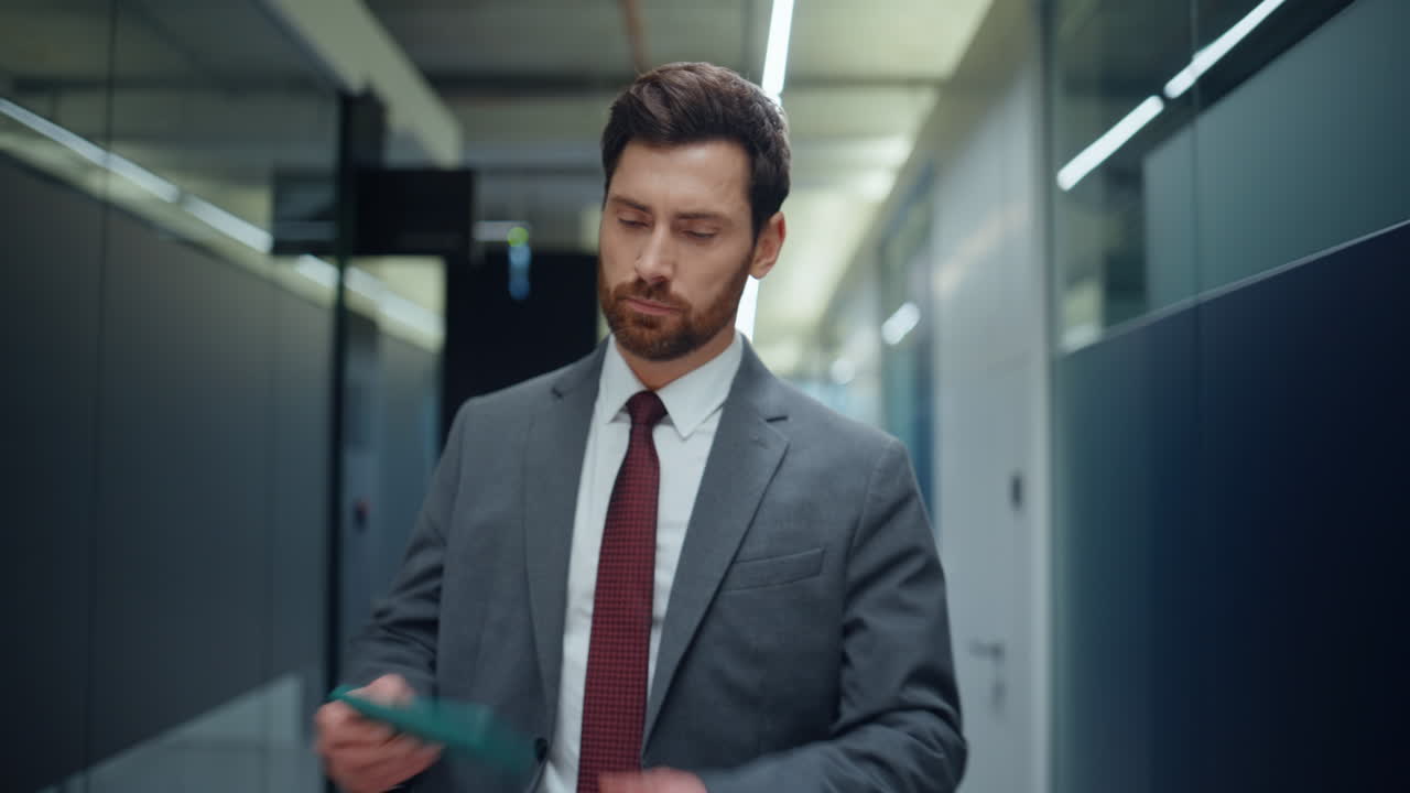Succesfuld leder, der spankulerer ned ad en korridor i en virksomhedsbygning og hilser pe folk tæt på.