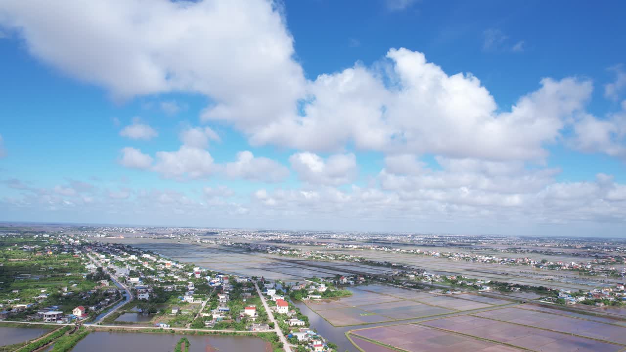 ベトナム北部のニンビン地方の田園地帯上空からのドローン空撮。広大な農地、小さな村、河川、そして大きな雲が浮かぶ青空の下の田園風景が映し出されている。