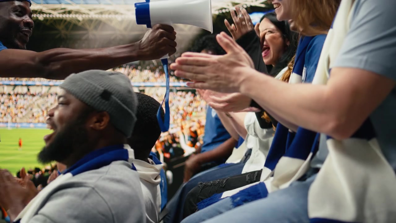 Diverse blue team soccer fans clapping and cheering from stands
