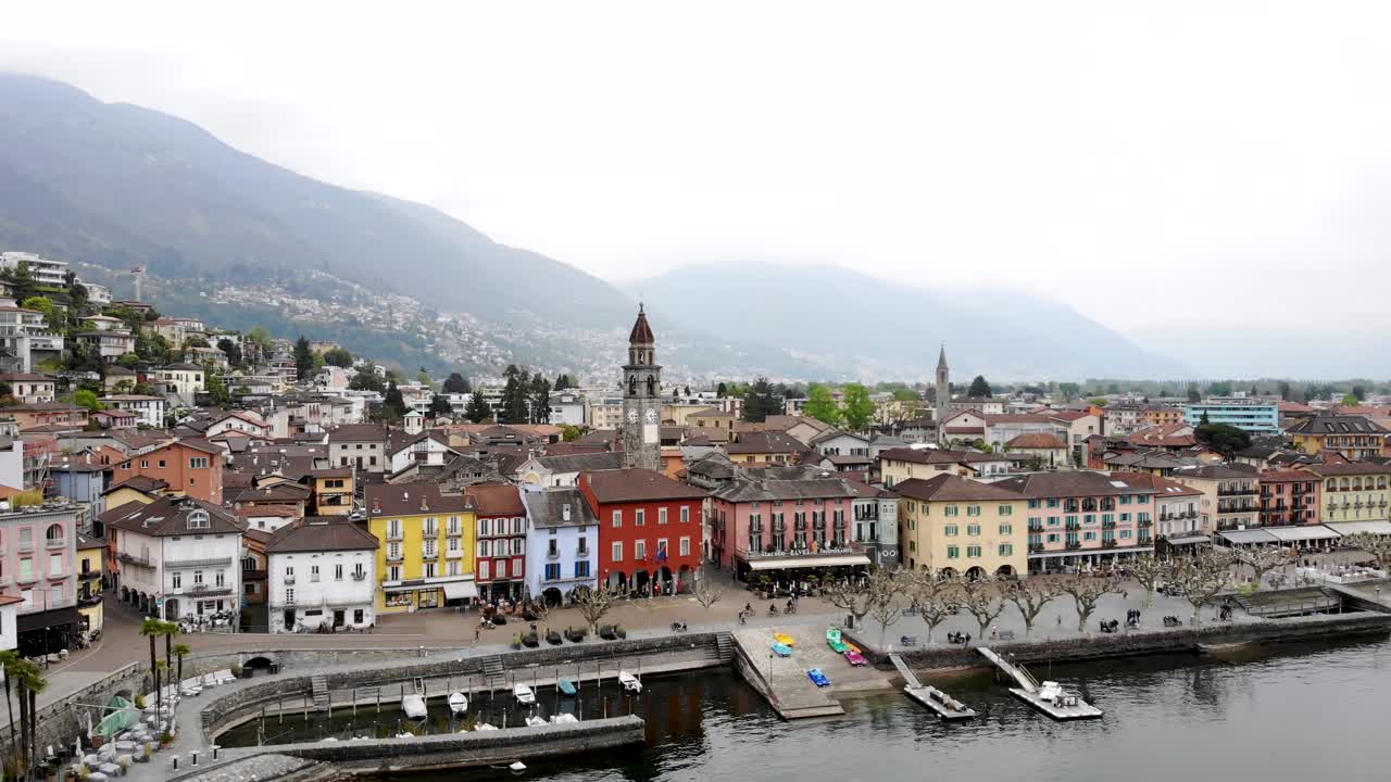 vista aérea de ascona en ticino, suiza en la orilla del lago maggiore con un movimiento de alejamiento que revela los tejados, el lago y las montañas en el fondo desde una elevación más alta
