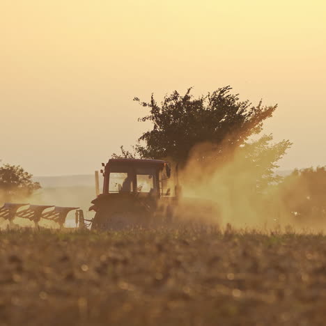 Agricultural machine cultivates the soil on natural dust background. Tractor working on the field in the morning outdoors.