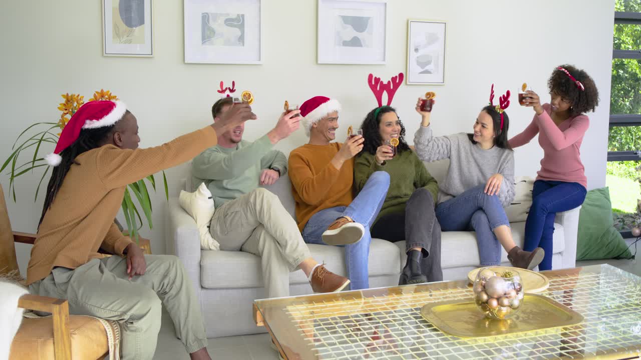 Diverse group of six friends raising cocktail glasses in holiday living room after glass extension