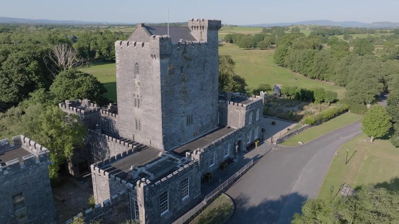 Una casa torre medievale in pietra si erge accanto a un vialetto curvo e vuoto in mezzo alla aperta campagna irlandese in pieno giorno