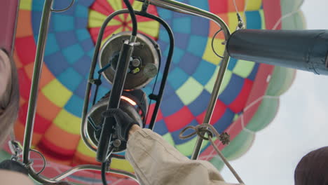 close up of hand tightly gripping braided rope inside woven wicker basket, denim fabric visible beside black leather cushion, suggesting tension or support during balloon ride under soft daylight