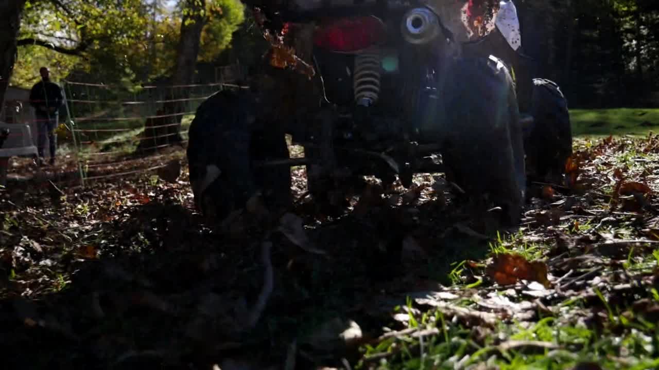 Primo piano di un quad in slow motion con un bambino alla guida che fa derapate, spruzzando fango e foglie verso la telecamera.