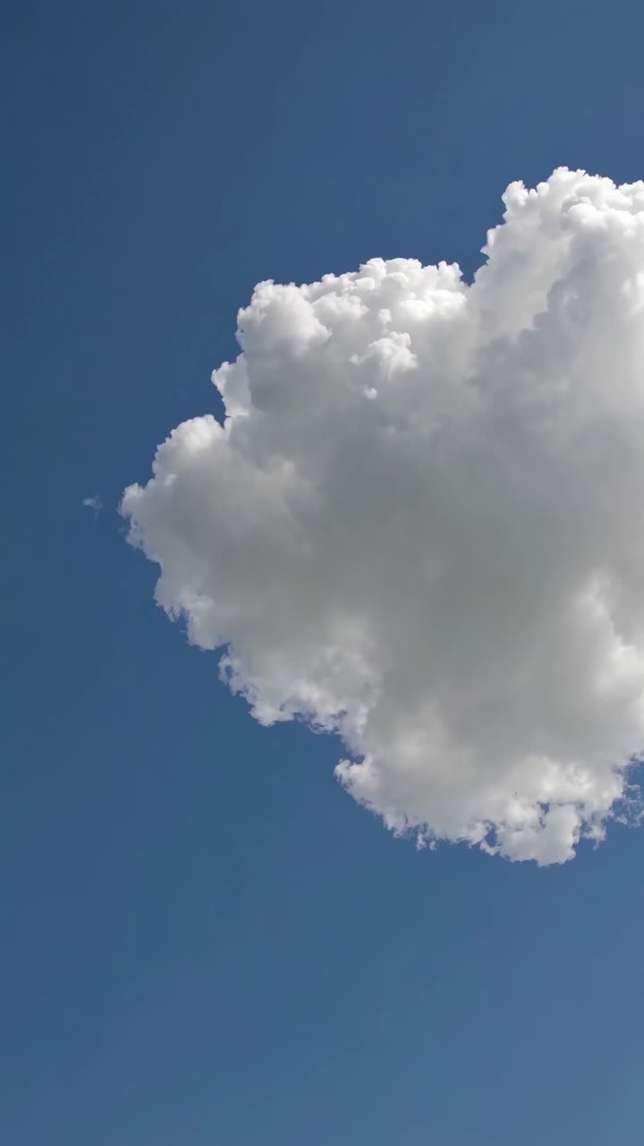 A low-angle video shot captures a fluffy white cloud against a clear blue sky, emphasizing a serene