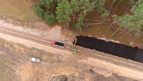 Excavadora-Amarilla-Y-Camión-Volquete-Trabajando-En-La-Construcción-De-Carreteras,-Vista-Aérea-De-Arriba-Hacia-Abajo