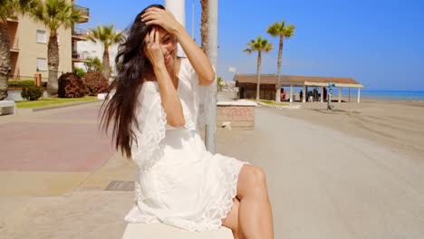 Brunette-Woman-Sitting-on-Beach-Promenade-Wall