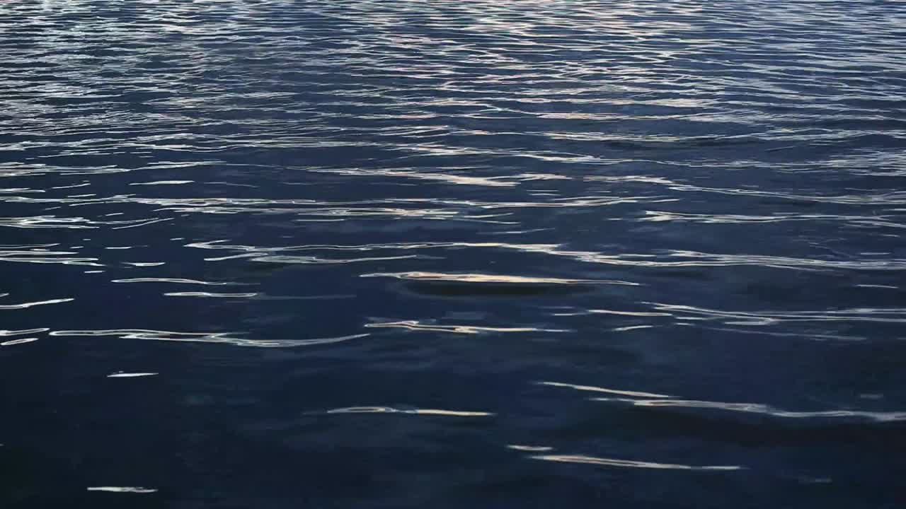 Quiet evening next to a blue water bay; dark, calm and cool water radiates peace; ripples reflect grey light. Sun has set. Footage in HD