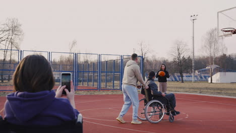 disabled woman in wheelchair recording with smartphone to her friends playing to basketball 1