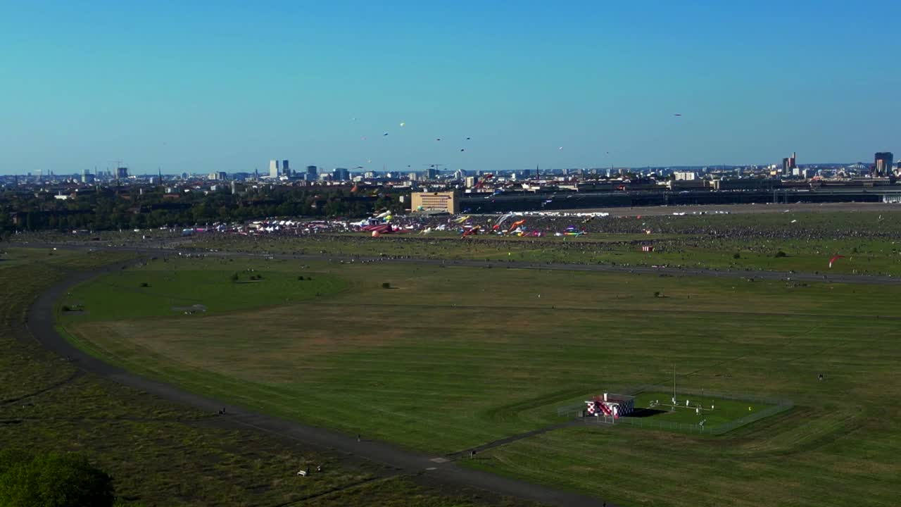thousands of Berliners enjoying the giant kite festival on a sunny day at Tempelhofer Feld, the former Tempelhof Airport. Best aerial view flight descending drone