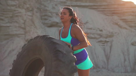 girl on a sand quarry pushing a wheel in training crossfit workout at sunset in the sun