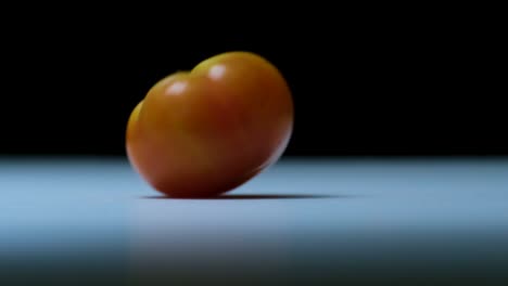 a-tomato-rolling-on-table-on-black-background,-copy-space