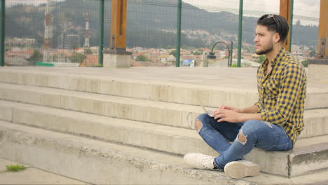 Handsome-man-siting-on-stairs-using-laptop-outdoors