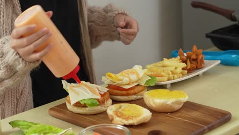 Frau-Gibt-In-Der-Küche-Senfsauce-Auf-Hausgemachte-Burger-Mit-Salat,-Käse,-Tomaten-Und-Schinken