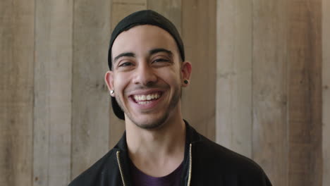 Primer-Plano-Retrato-De-Un-Atractivo-Joven-Hispano-Estudiante-Sonriendo-Feliz-Sorpresa-Mirando-La-Cámara-Alegre-Adolescente-Con-Sombrero-Fondo-De-Madera