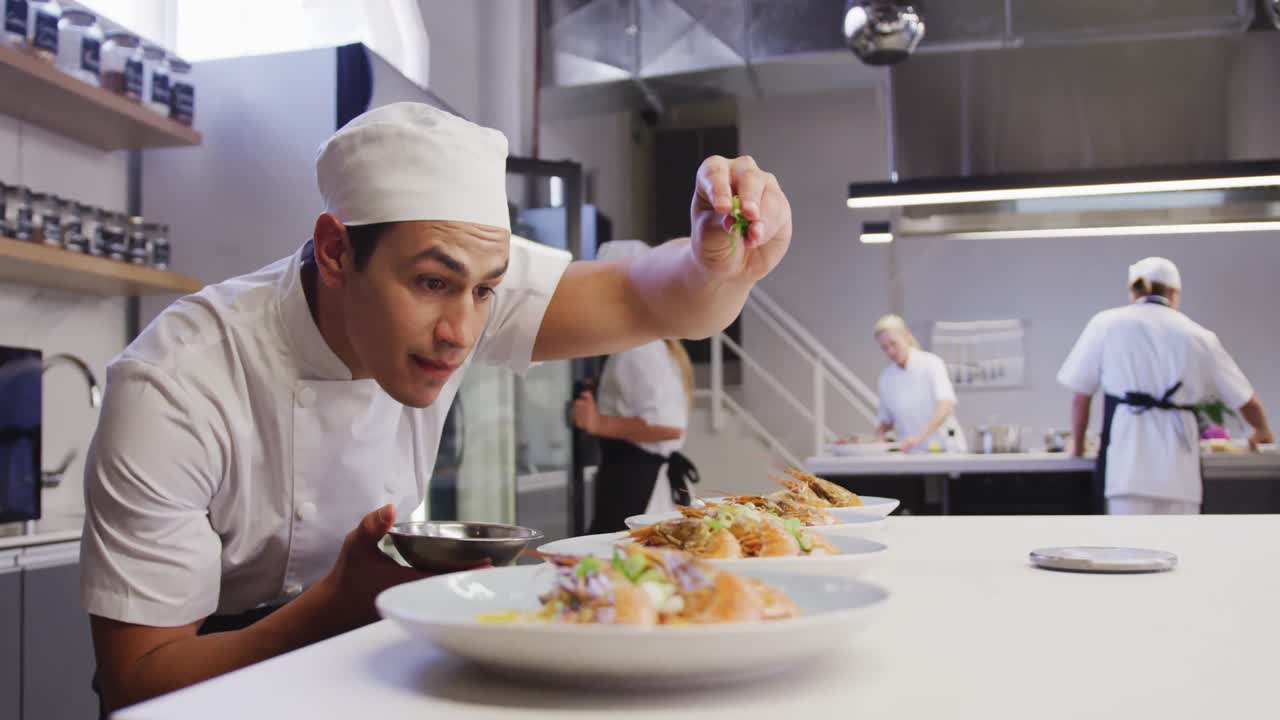 cocinero profesional de raza mixta en una cocina de un restaurante, poniendo comida en un plato
