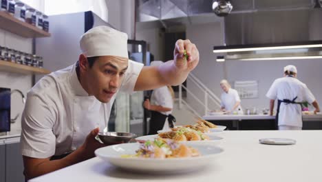 Professional-mixed-race-male-chef-in-a-restaurant-kitchen,-putting-food-on-a-plate
