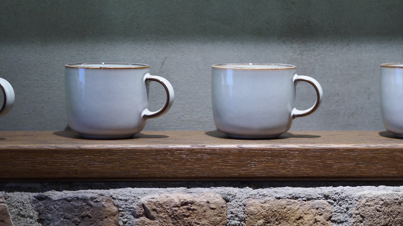 Ceramic Mugs Displayed on a Wooden Shelf Above a Brick Wall
