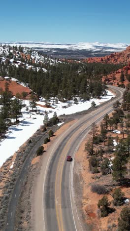red car driving on a scenic winding road through snow-covered red rock landscape