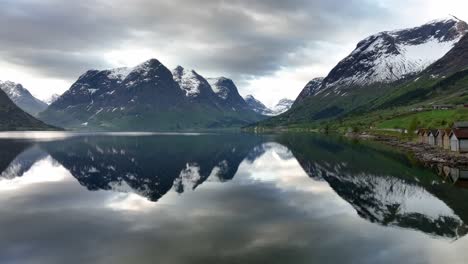 Fyling-forward-close-to-glacial-Opstrynsvatnet-lake-water-surface---Tall-mountains-containing-jostedal-glacier---Aerial-with-beautiful-reflections-in-water